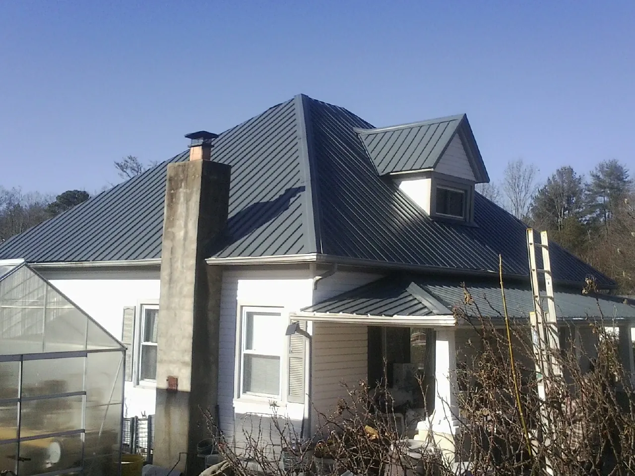 Dark blue standing seam metal roof on a white farmhouse with dormer — Slate & Tile Roof Repair by Roofing Brothers in Cedarhurst