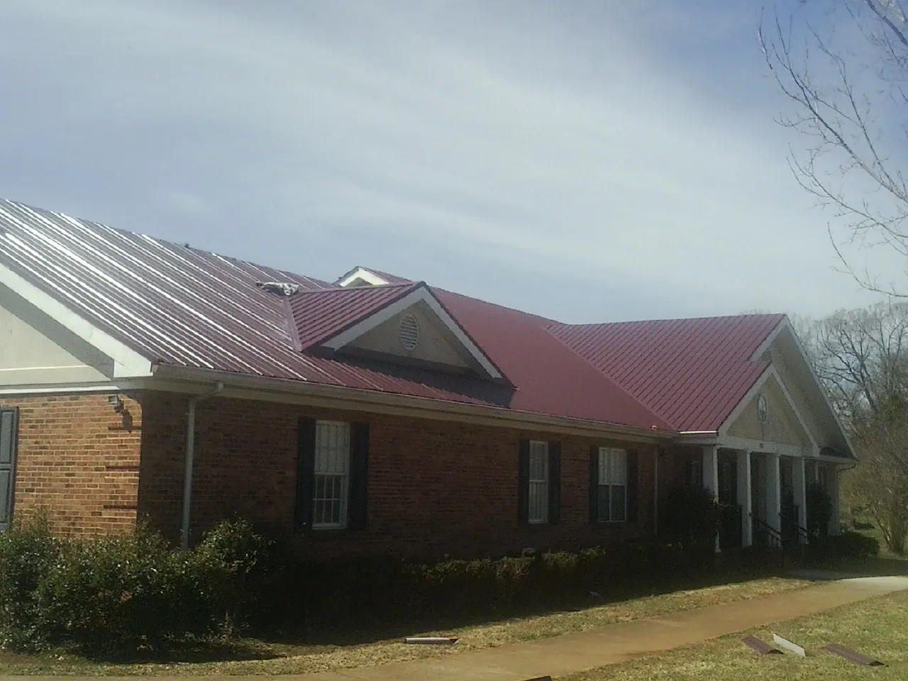 Red metal roof with gabled entries on a long brick building, from a Hail Damage Roof Repair job in Cedarhurst