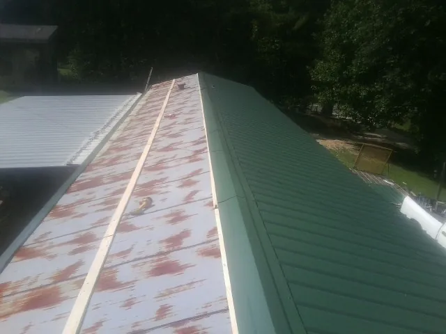 Old rusted panels beside newly installed green metal roofing — Wind Damage Roof Repair by Roofing Brothers in Cedarhurst