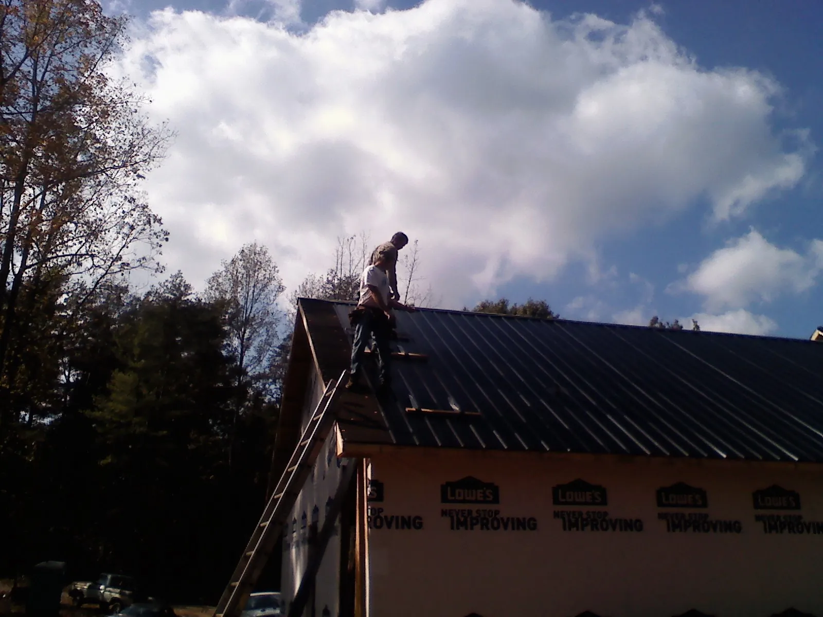 Roofer fastening dark metal panels high against a cloudy sky, from a Roof Inspection job in Cedarhurst