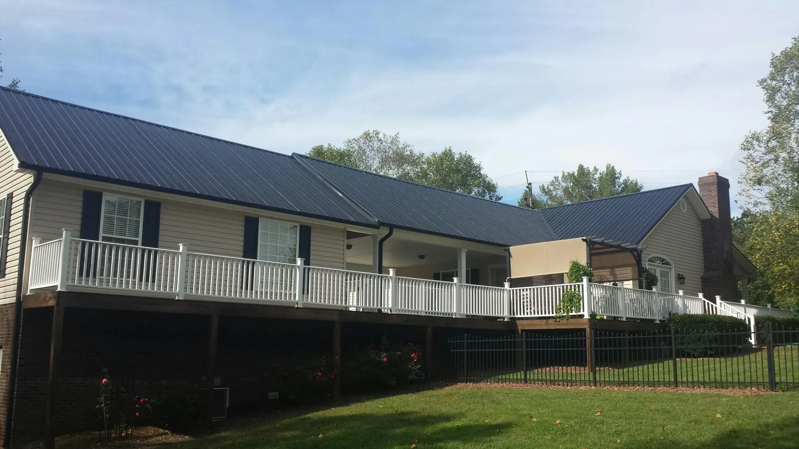 Black metal roof above a long white railed deck on a hillside home in Cedarhurst