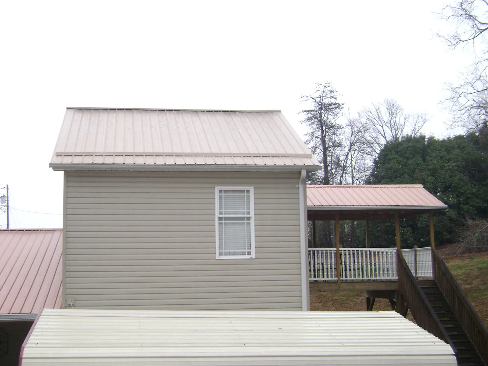 Tan metal roofs on a two story addition and attached porch, from a Roof Replacement job in Cedarhurst
